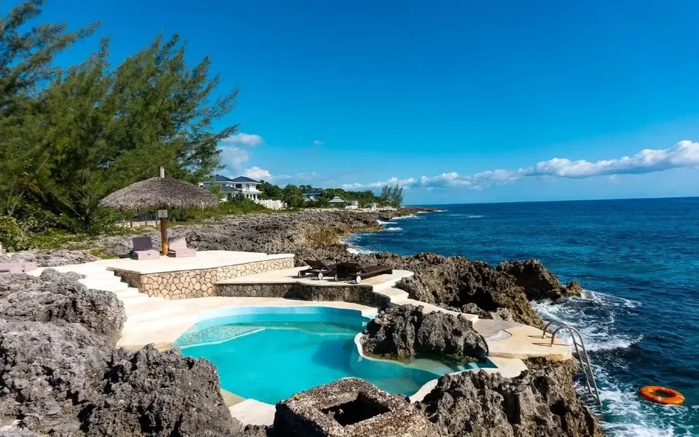 Natural stone pool by the ocean with lounge chairs and clear blue water